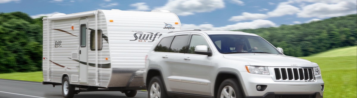 A silver Jeep® hauling a Jayco® Swift RV trailer on a scenic route. 